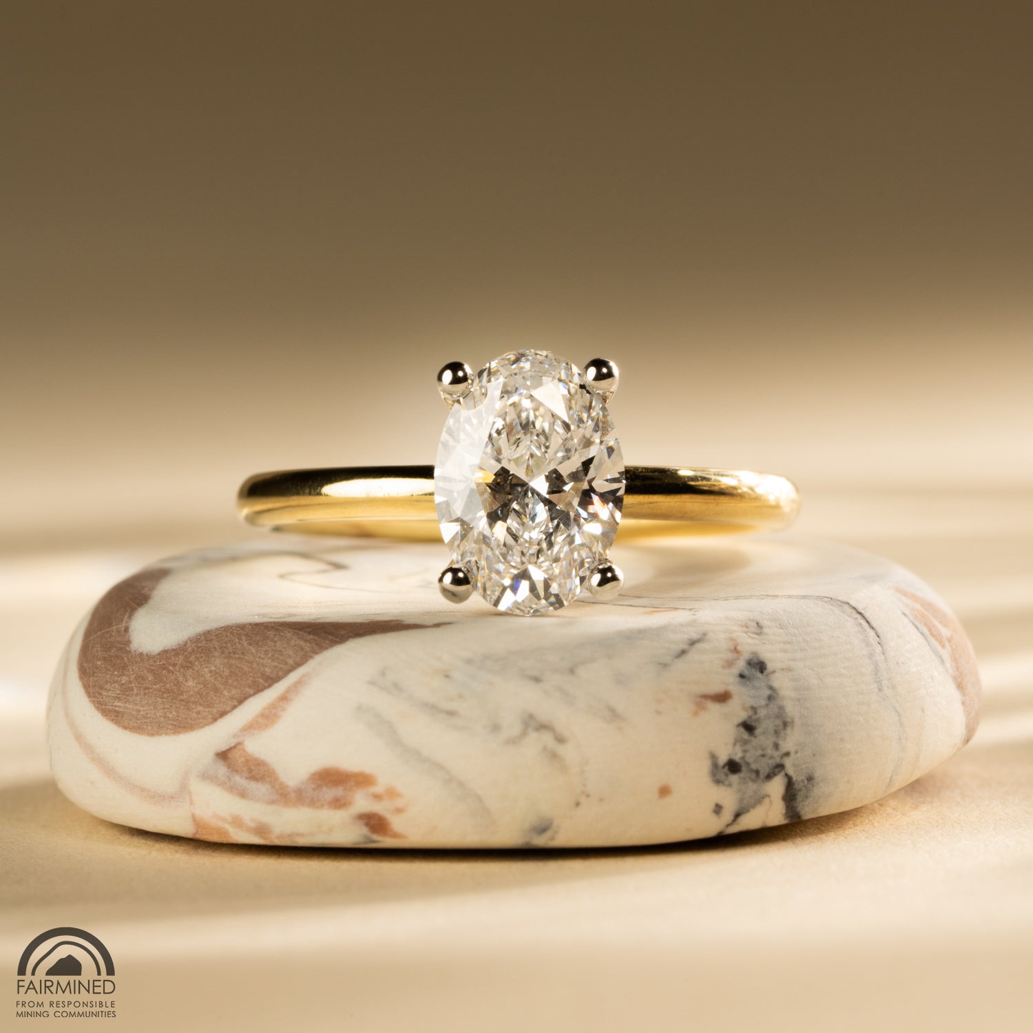 An oval cut diamond in a white gold prong setting, on a yellow gold band.